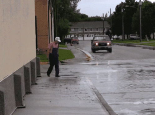 A Man Walking Down A Sidewalk In The Rain With A Red Truck Behind Him GIF