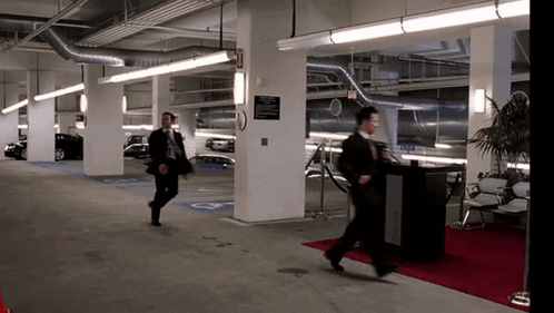 A Man Walking In A Parking Garage With A Sign On The Wall That Says ' Exit ' GIF
