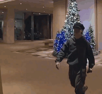 A Man Walking In Front Of A Building With Christmas Trees GIF
