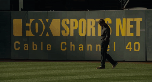 A Man Walking On A Baseball Field In Front Of A Fox Sports Net Cable Channel 40 Sign GIF