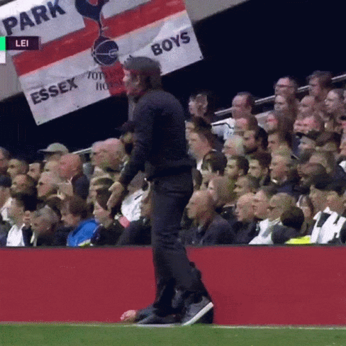A Man Walking On A Soccer Field With A Banner That Says Essex Boys GIF