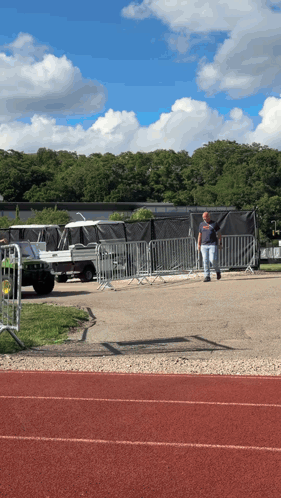 A Man Walking On A Track In Front Of A Fence With A Jeep In The Background GIF