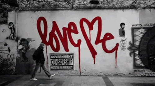 A Man Walks Past A Wall That Has Graffiti On It That Says Love GIF
