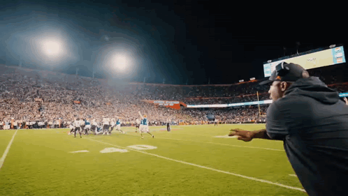 A Man Watches A Football Game In A Stadium With A Scoreboard That Says ' Nfl ' On It GIF