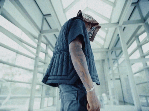 A Man Wearing A Bandana And A Black Vest Looks Down GIF