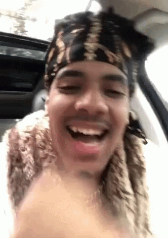 A Man Wearing A Bandana And A Fur Coat Is Sitting In A Car And Smiling . GIF