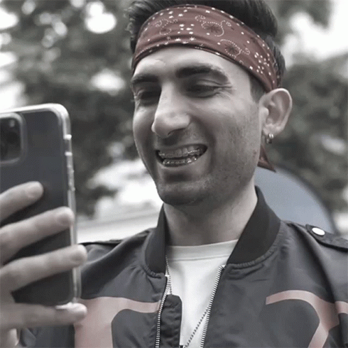 a man wearing a bandana and braces takes a selfie with his phone