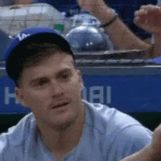 A Man Wearing A Baseball Cap And A Blue Shirt Is Sitting In The Dugout . GIF