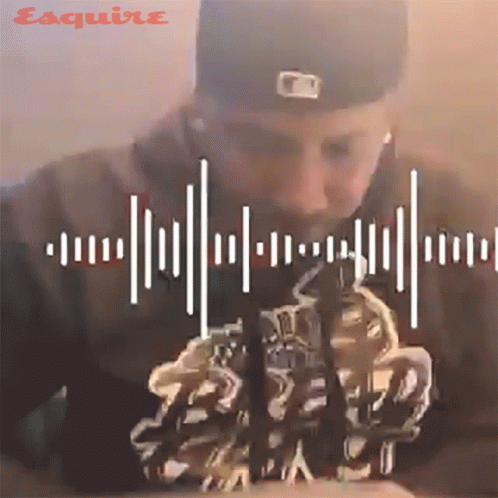 A Man Wearing A Baseball Cap And Ear Buds Looks Down At Something With Esquire Written On The Bottom Right GIF