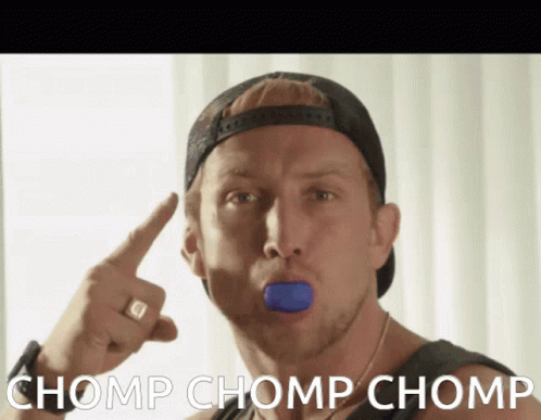 A Man Wearing A Baseball Cap Has A Blue Object In His Mouth And Says Chomp Chomp Chomp In White Letters GIF