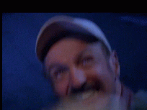 a man wearing a baseball cap is eating a sandwich in a blurry photo .