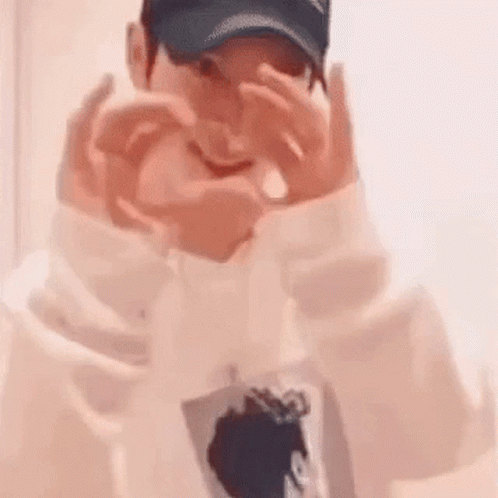 A Man Wearing A Baseball Cap Is Making A Heart With His Hands . GIF