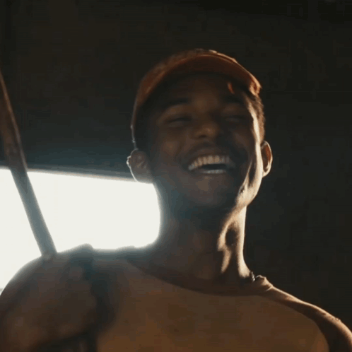 A Man Wearing A Baseball Cap Is Smiling And Holding A Stick GIF