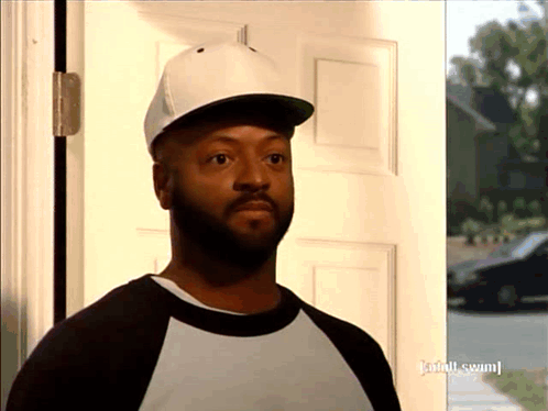 A Man Wearing A Baseball Cap Is Standing In Front Of A Door That Has Adult Swim Written On It GIF