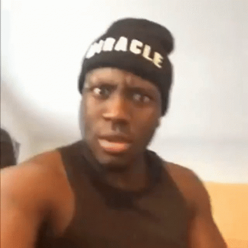 A Man Wearing A Beanie And A Black Tank Top Is Making A Funny Face . GIF