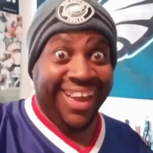 A Man Wearing A Beanie And A Purple Shirt Is Smiling . GIF