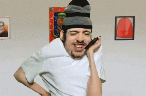 A Man Wearing A Beanie And A White Shirt Is Blowing Into A Straw GIF