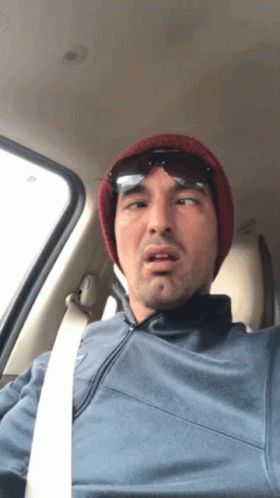 A Man Wearing A Beanie And Sunglasses Is Sitting In The Driver 'S Seat Of A Car GIF