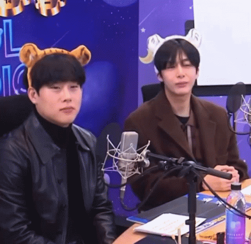 A Man Wearing A Bear Headband Sits Next To Another Man GIF