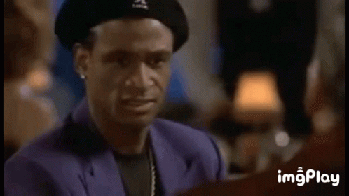 A Man Wearing A Beret And A Purple Suit Is Smiling While Talking To Another Man . GIF