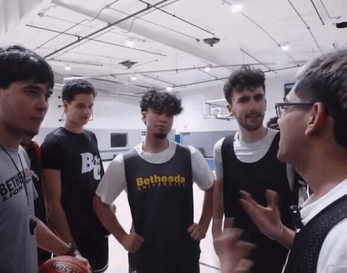 A Man Wearing A Bethesda University T-Shirt Talks To A Group Of Young Men GIF