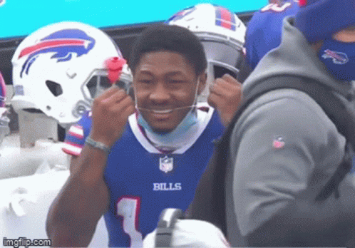 A Man Wearing A Bills Jersey Is Smiling And Putting On A Mask GIF
