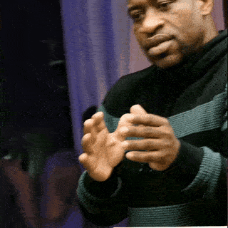 A Man Wearing A Black And Green Striped Sweater Holds His Hands Together GIF
