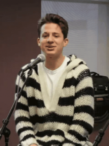 A Man Wearing A Black And White Striped Sweater Is Sitting In Front Of A Microphone GIF