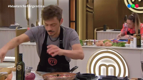 A Man Wearing A Black Apron With The Letter M On It GIF