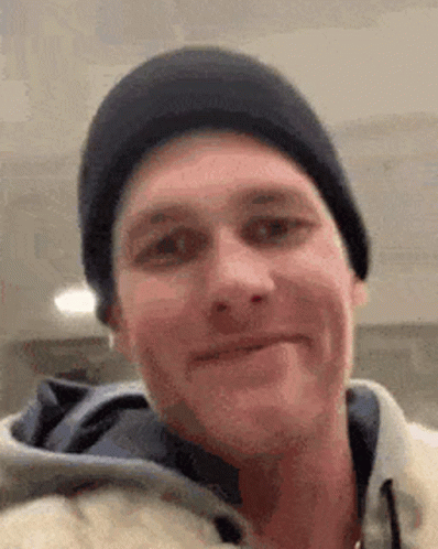A Man Wearing A Black Beanie And A Hoodie Is Smiling . GIF
