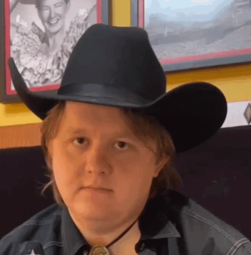 A Man Wearing A Black Cowboy Hat And A Star On His Shirt GIF