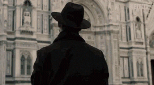 Man In Black Hat And Coat In Front Of Building GIF