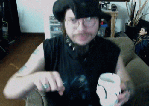 A Man Wearing A Black Hat And Glasses Is Holding A White Cup GIF