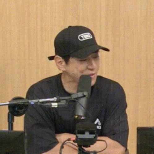 A Man Wearing A Black Hat Is Sitting In Front Of A Microphone And Talking Into It . GIF