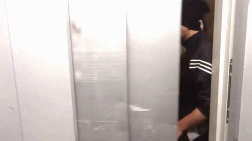 A Man Wearing A Black Hat Is Standing In A Doorway . GIF