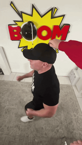 A Man Wearing A Black Hat Stands In Front Of A Boom Sign GIF