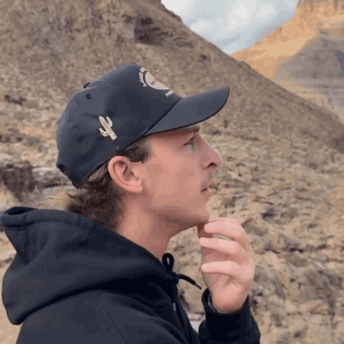 A Man Wearing A Black Hat With A Cactus On It Looks To The Side GIF