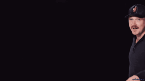 A Man Wearing A Black Hat With A Woman On It Making A Peace Sign GIF