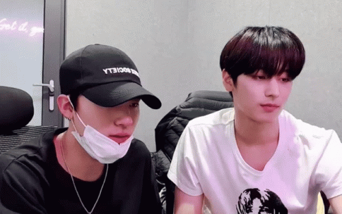 A Man Wearing A Black Hat With The Word Yt3 On It Sits Next To Another Man Wearing A Mask GIF