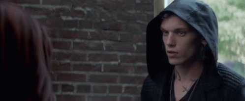 A Man Wearing A Black Hooded Jacket Has A Cross Tattoo On His Neck GIF
