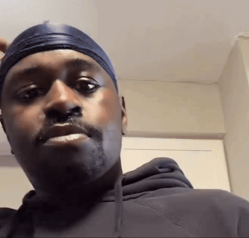 A Man Wearing A Black Hoodie And A Headband Looks At The Camera GIF