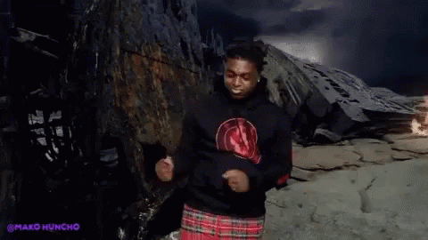 A Man Wearing A Black Hoodie And A Plaid Skirt Is Dancing In Front Of A Mountain . GIF