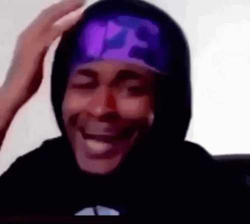 A Man Wearing A Black Hoodie And A Purple Hat Is Smiling And Touching His Head . GIF