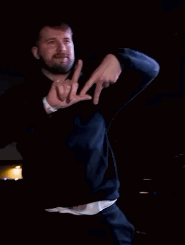 A Man Wearing A Black Hoodie Is Making A Hand Gesture With His Fingers GIF