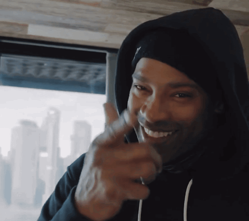 A Man Wearing A Black Hoodie Is Smiling And Pointing His Finger GIF