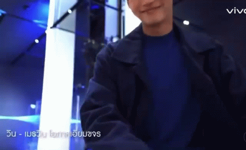 A Man Wearing A Black Jacket And A Blue Shirt Is Standing In A Room . GIF