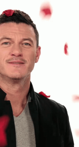 A Man Wearing A Black Jacket And A Grey Shirt With Red Roses On His Head GIF