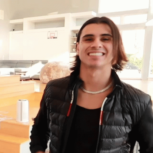 A Man Wearing A Black Jacket And A Necklace Smiles GIF