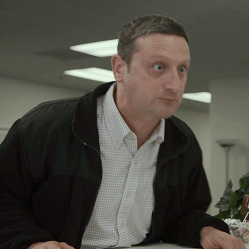 A Man Wearing A Black Jacket And A Plaid Shirt Looks At Something GIF