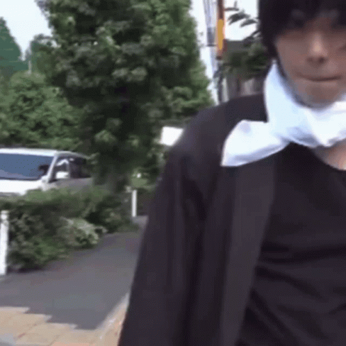A Man Wearing A Black Jacket And A White Scarf Around His Neck Is Walking Down The Street . GIF